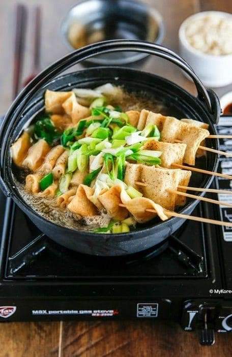 Skewered tofu with green onions being cooked on a portable stove.