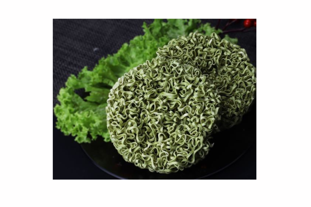 Green noodles on a black plate with green leaves