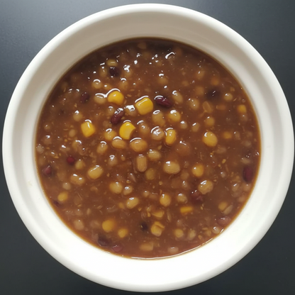 White bowl filled with a brown soup containing corn and beans on a dark background