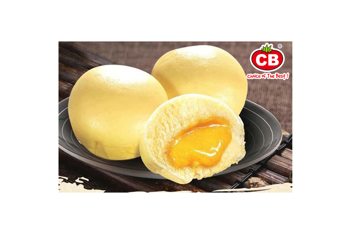 Three yellow pastries on a dark plate with one cut open to reveal a filling, branded 'CB'.