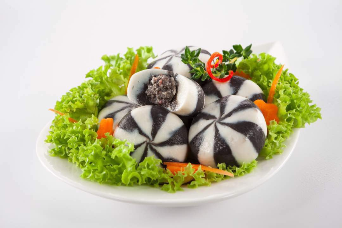Decorative black and white patterned food item on a bed of green lettuce with carrots on a white plate.