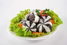 Decorative black and white patterned food item on a bed of green lettuce with carrots on a white plate.