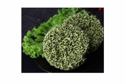 Green noodles on a black plate with green leaves